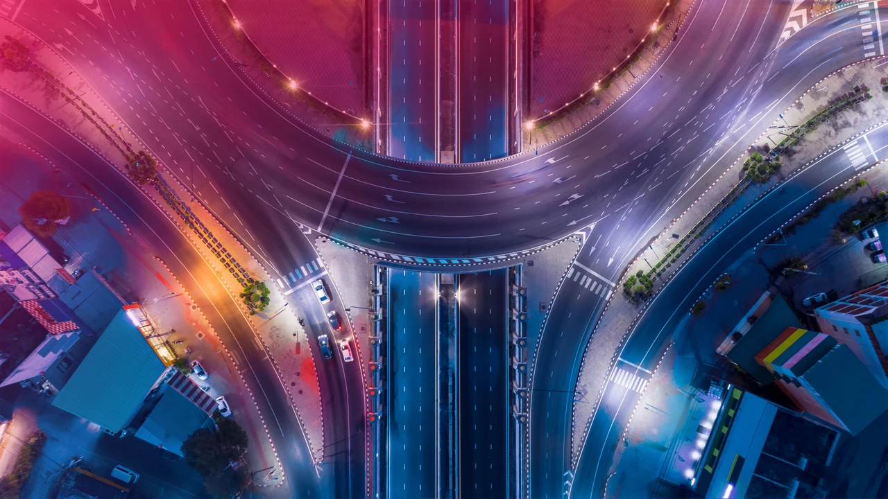 Aerial view of a brightly lit, empty city intersection at night, with curved roads and colorful lighting in pink, orange, and blue hues—an image that captures the complexity and organization akin to expert portfolio management.