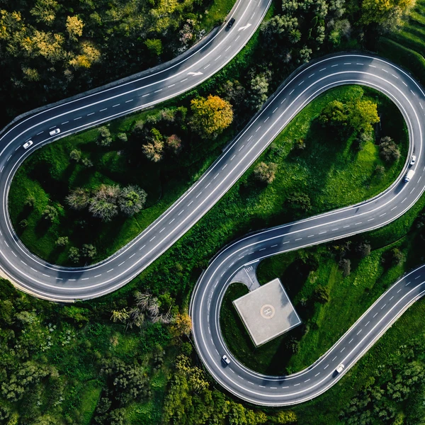 Aerial view of cars driving on a winding S-shaped road surrounded by green trees and grass, with a helipad near the curve—an image that evokes strategic navigation and precision, much like effective portfolio management.